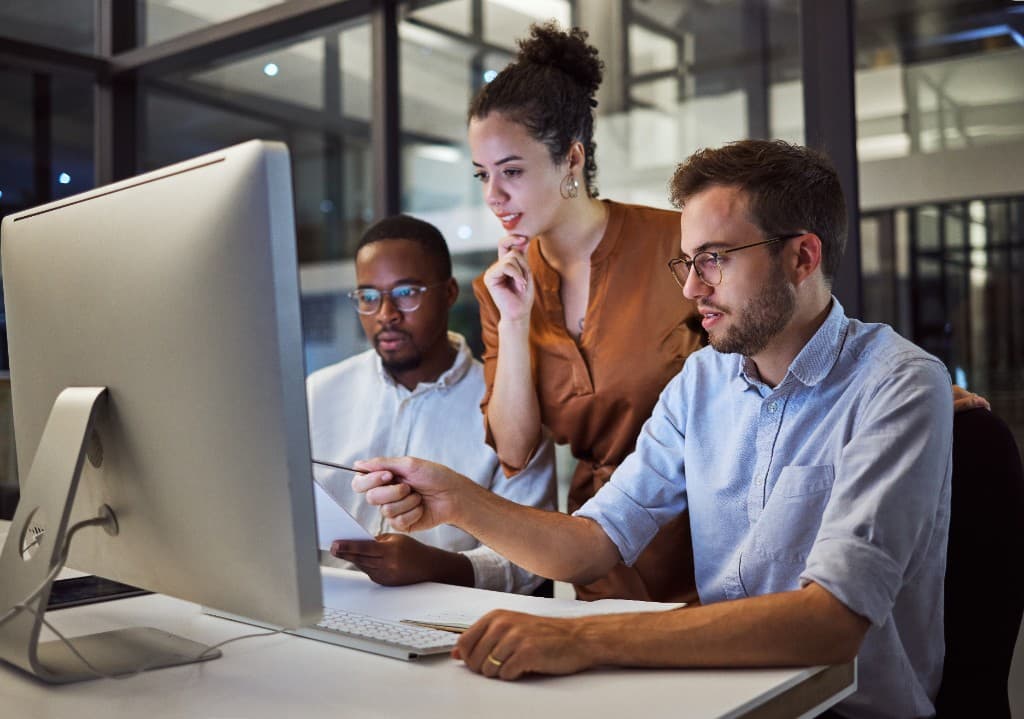 Three diverse professionals collaborating and looking at a computer screen in a modern office