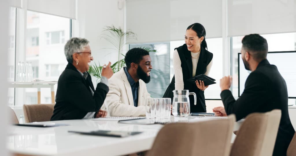 A diverse team of four professionals laughing and collaborating during a meeting in a bright, modern office