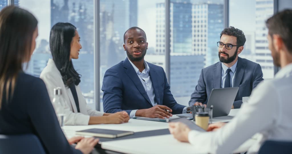 A diverse group of business professionals meeting in a modern glass-walled office overlooking a city skyline